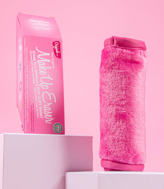 Rolled up Original Pink MakeUp Eraser next to packaging, both propped up on platforms.