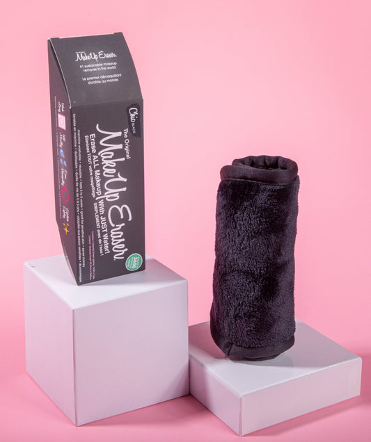Rolled up Chic Black MakeUp Eraser next to packaging, both propped up on platforms.