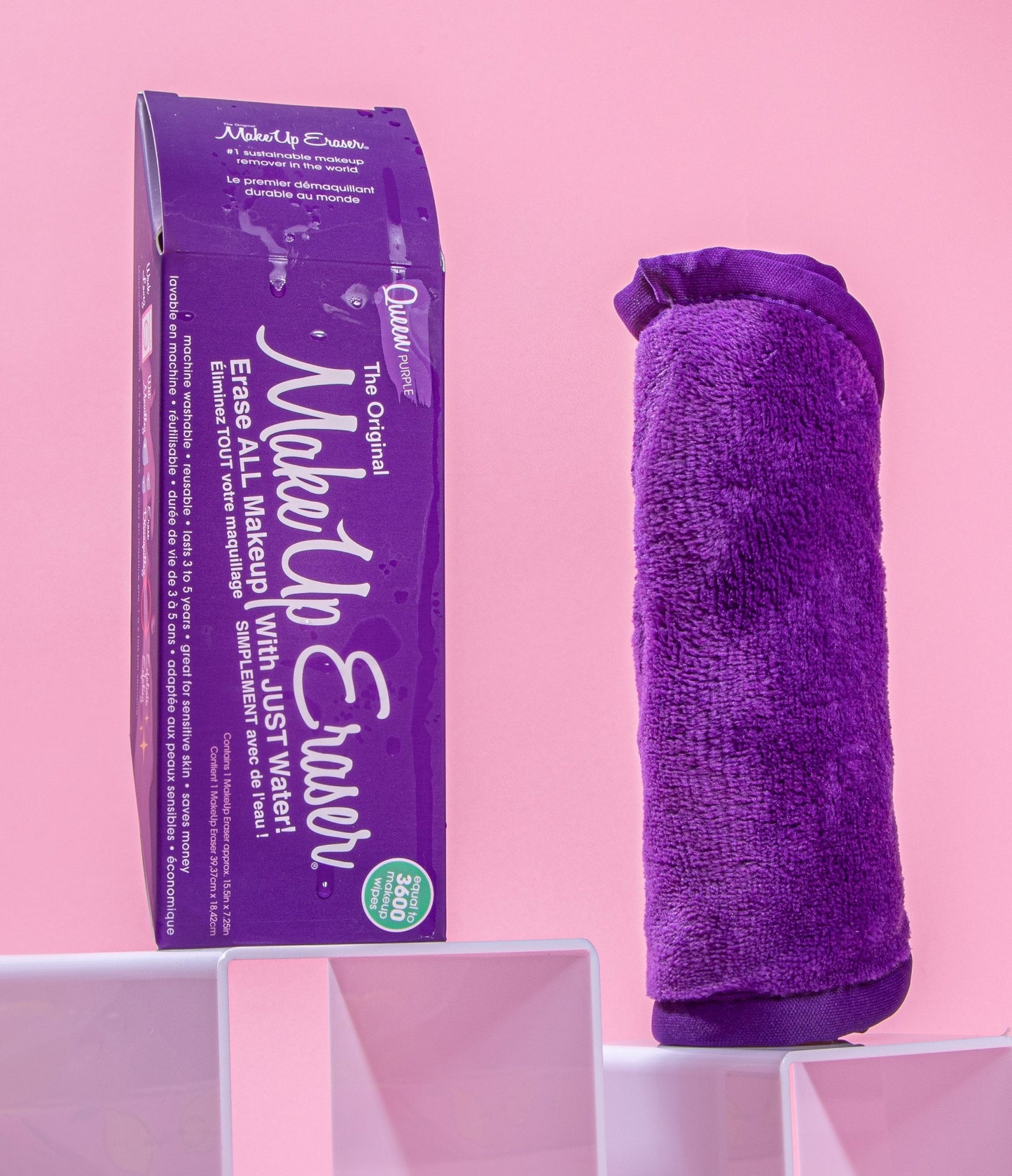 Rolled up Queen Purple MakeUp Eraser next to packaging, both propped up on platforms.