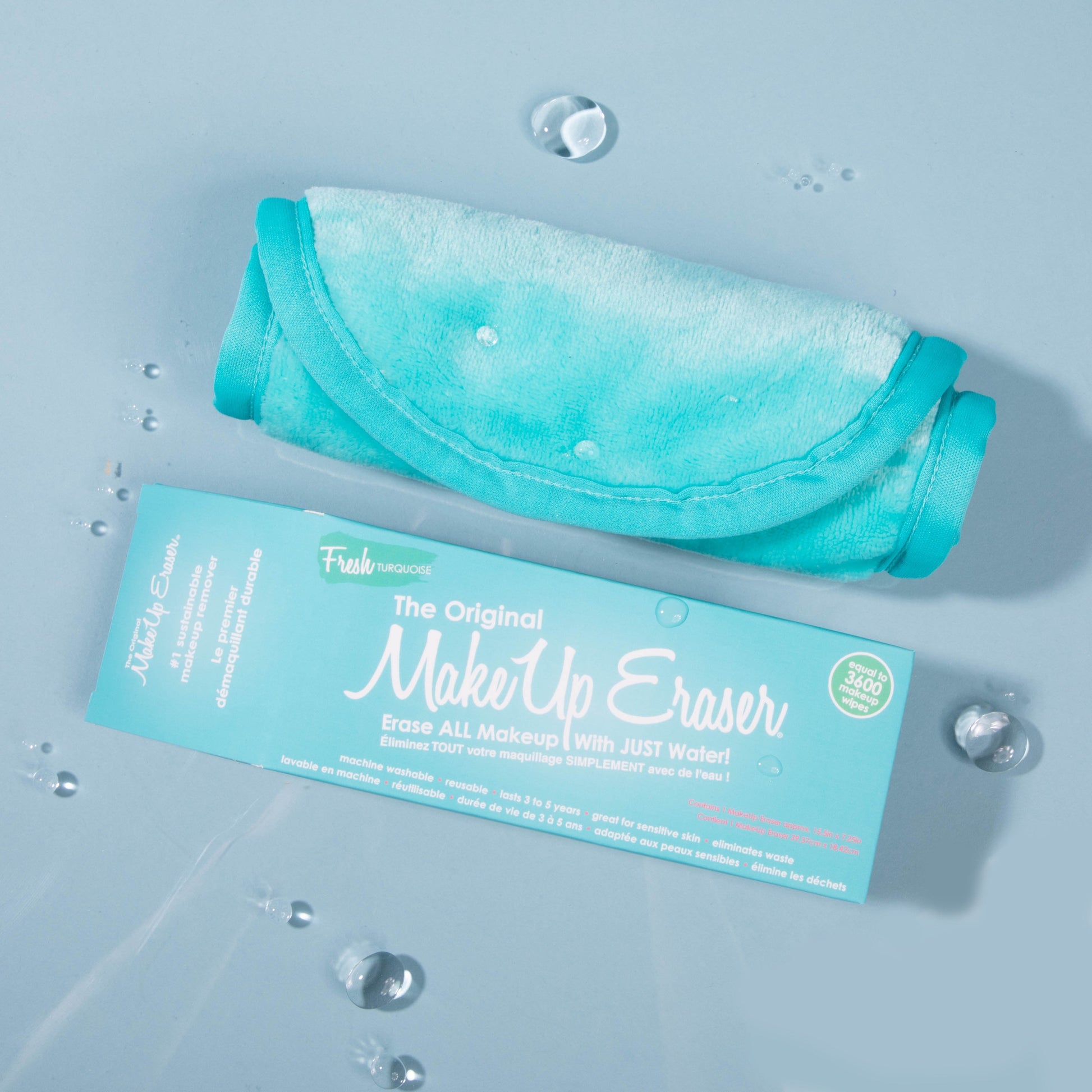 Rolled up Fresh Turquoise MakeUp Eraser next to packaging surrounded by water drops.