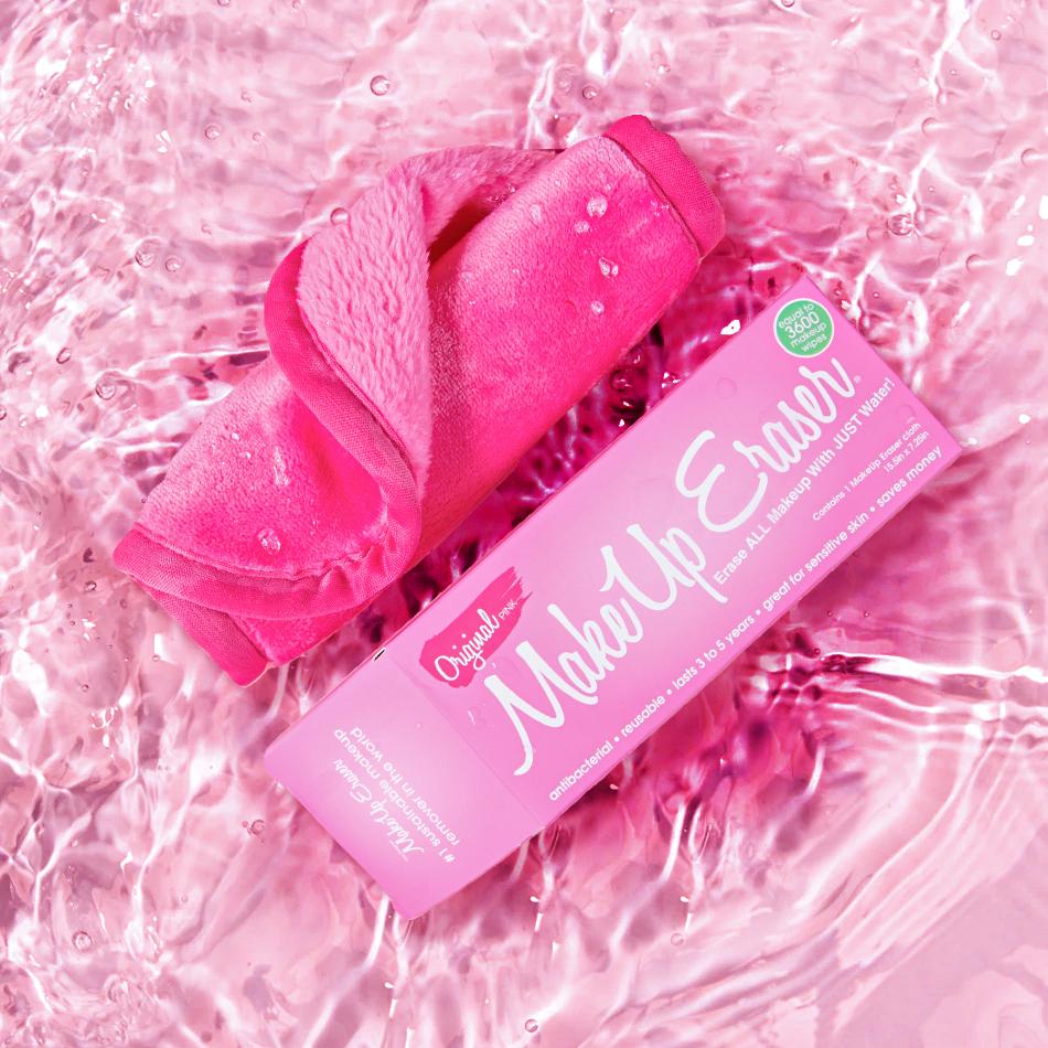 Rolled up Original Pink MakeUp Eraser next to packaging surrounded by water.