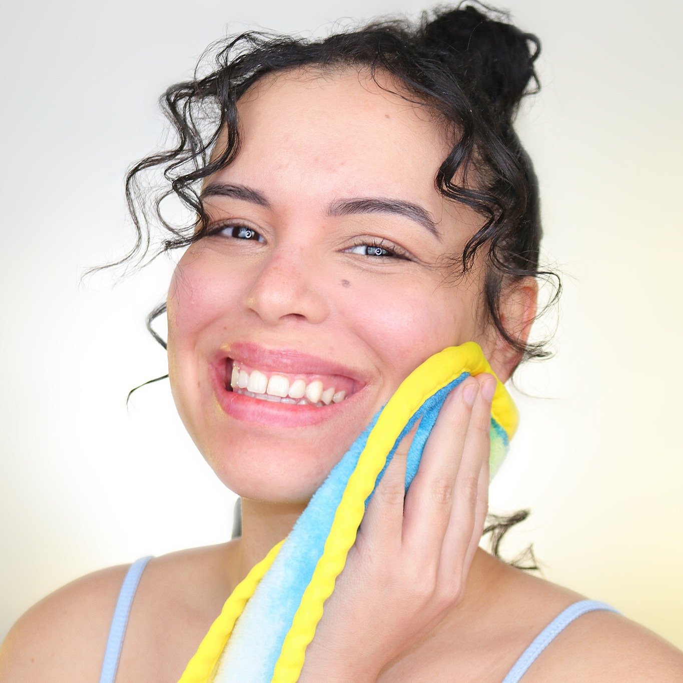 Woman smiling and holding charity: water MakeUp Eraser up to her face.