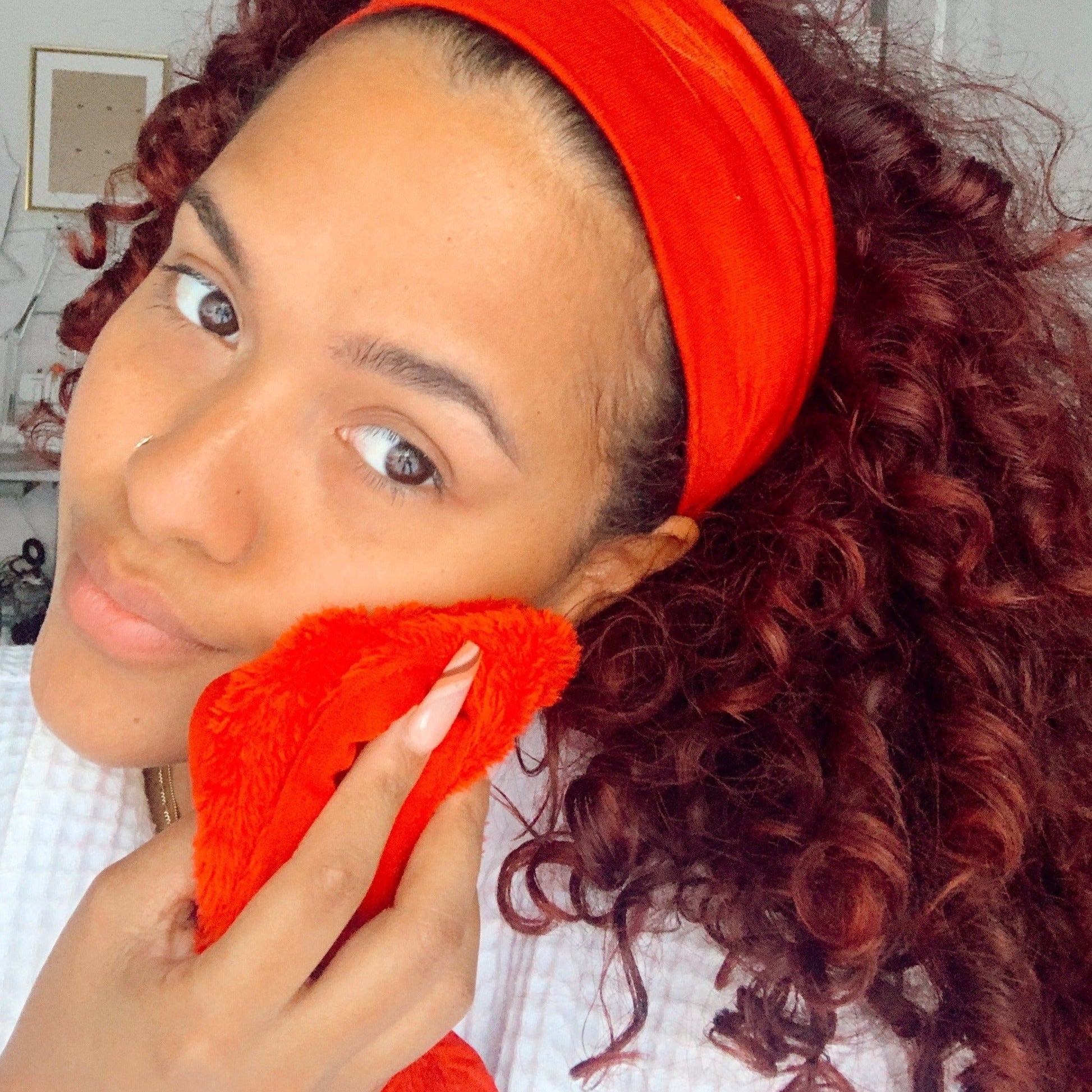 Woman holding up Love Red MakeUp Eraser cloth to face.